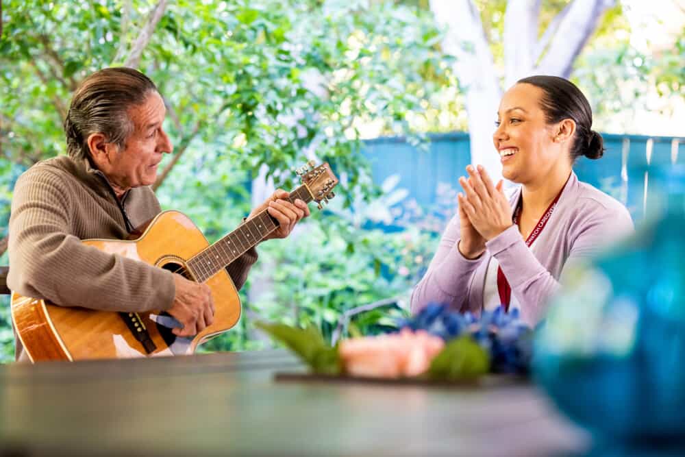 woman clapping to older man playing guitar outside